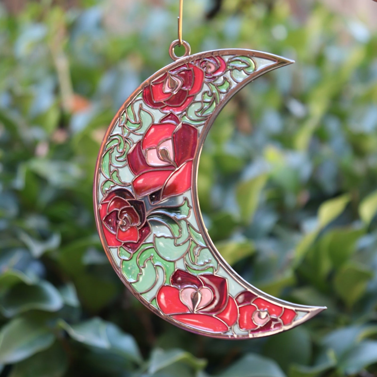 Someone holding the Moon Roses Witchy Christmas Ornament in front of a green bush.