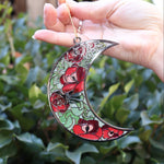 Someone holding the Moon Roses Witchy Christmas Ornament in front of a green bush.