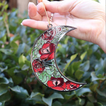 Someone holding the Moon Roses Witchy Christmas Ornament in front of a green bush.