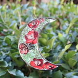 Someone holding the Moon Roses Witchy Christmas Ornament in front of a green bush.