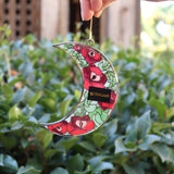 Someone holding the Moon Roses Witchy Christmas Ornament in front of a green bush, showing off the back.