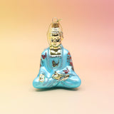The blue Buddha with Butterfly Glass Ornament on a pink and yellow background.