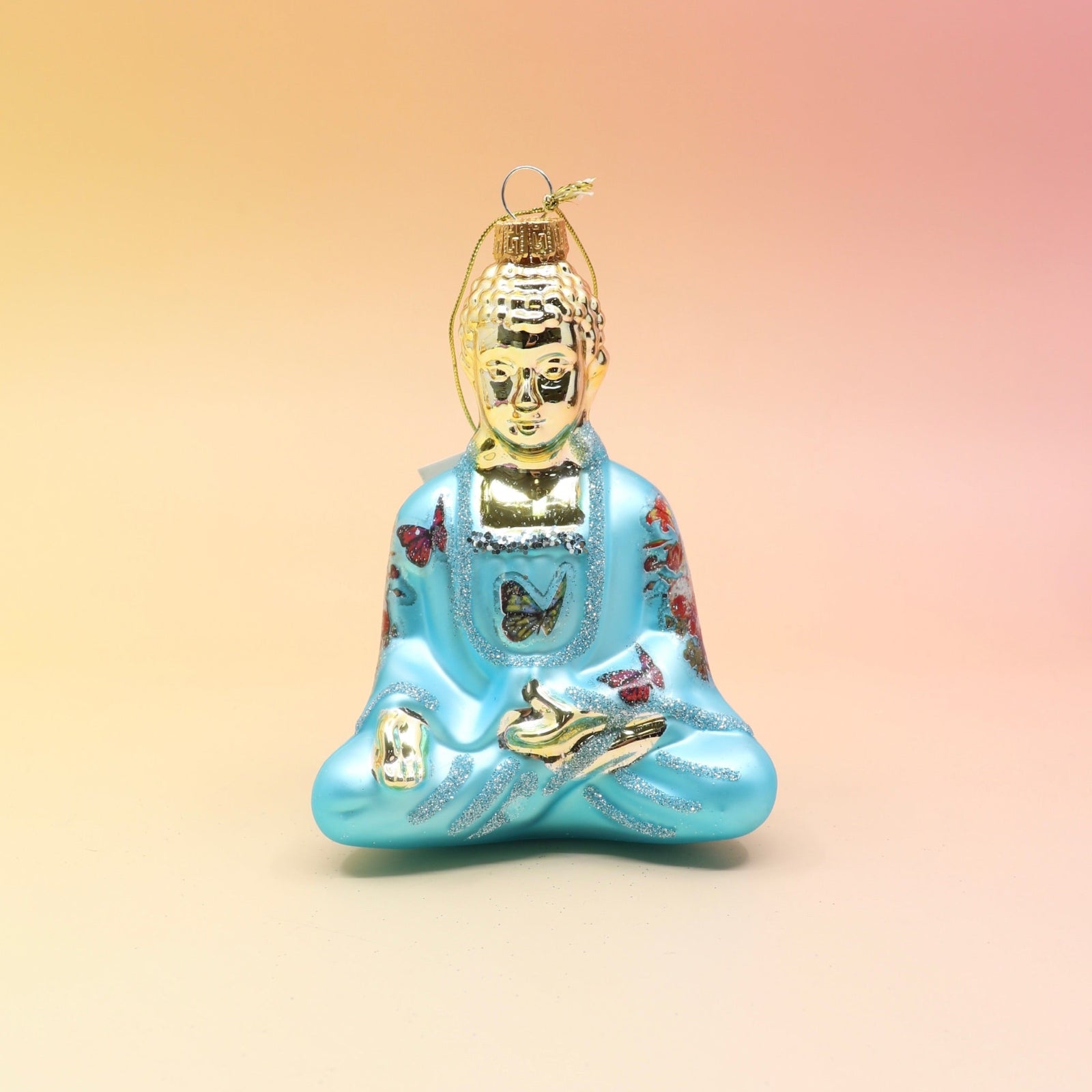 The blue Buddha with Butterfly Glass Ornament on a pink and yellow background.