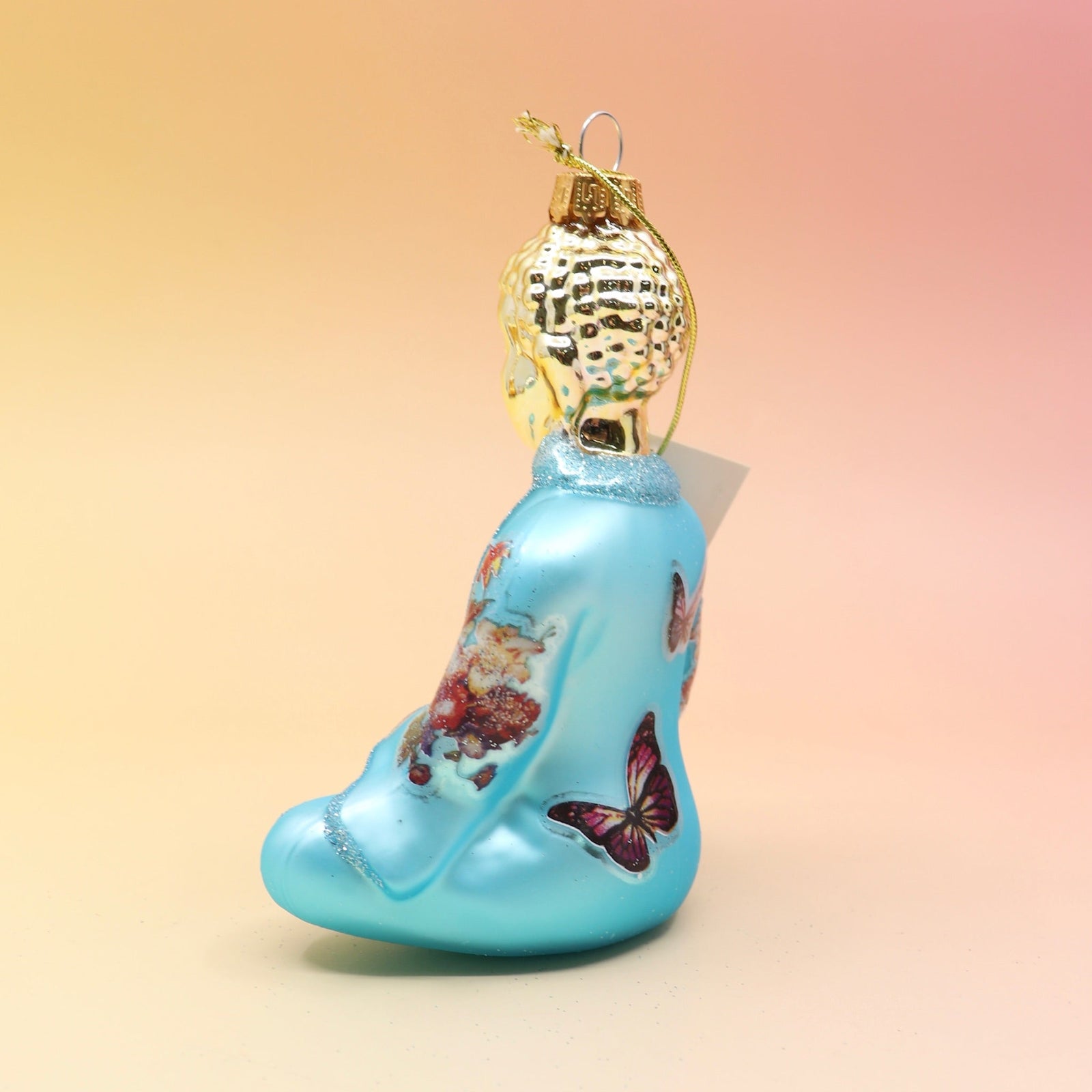 The blue Buddha with Butterfly Glass Ornament on a pink and yellow background, showing off the side.