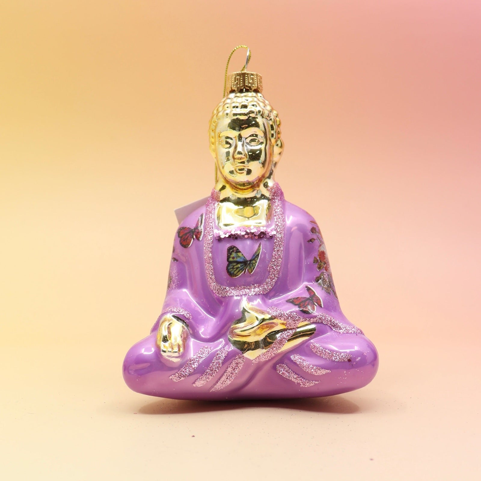 The pink Buddha with Butterfly Glass Ornament on a pink and yellow background.