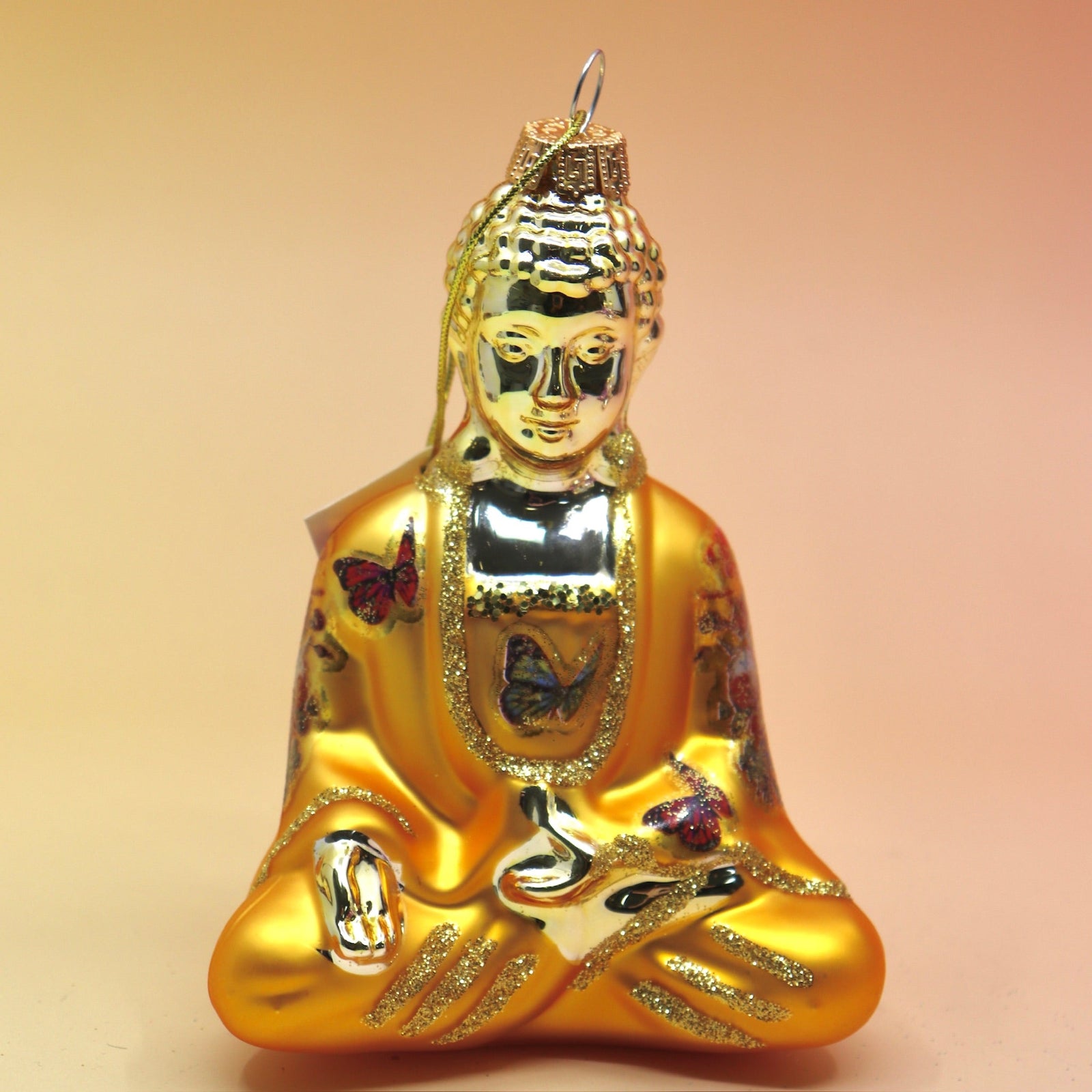 The orange Buddha with Butterfly Glass Ornament on a pink and yellow background.