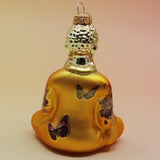 The orange Buddha with Butterfly Glass Ornament on a pink and yellow background, showing off the back.