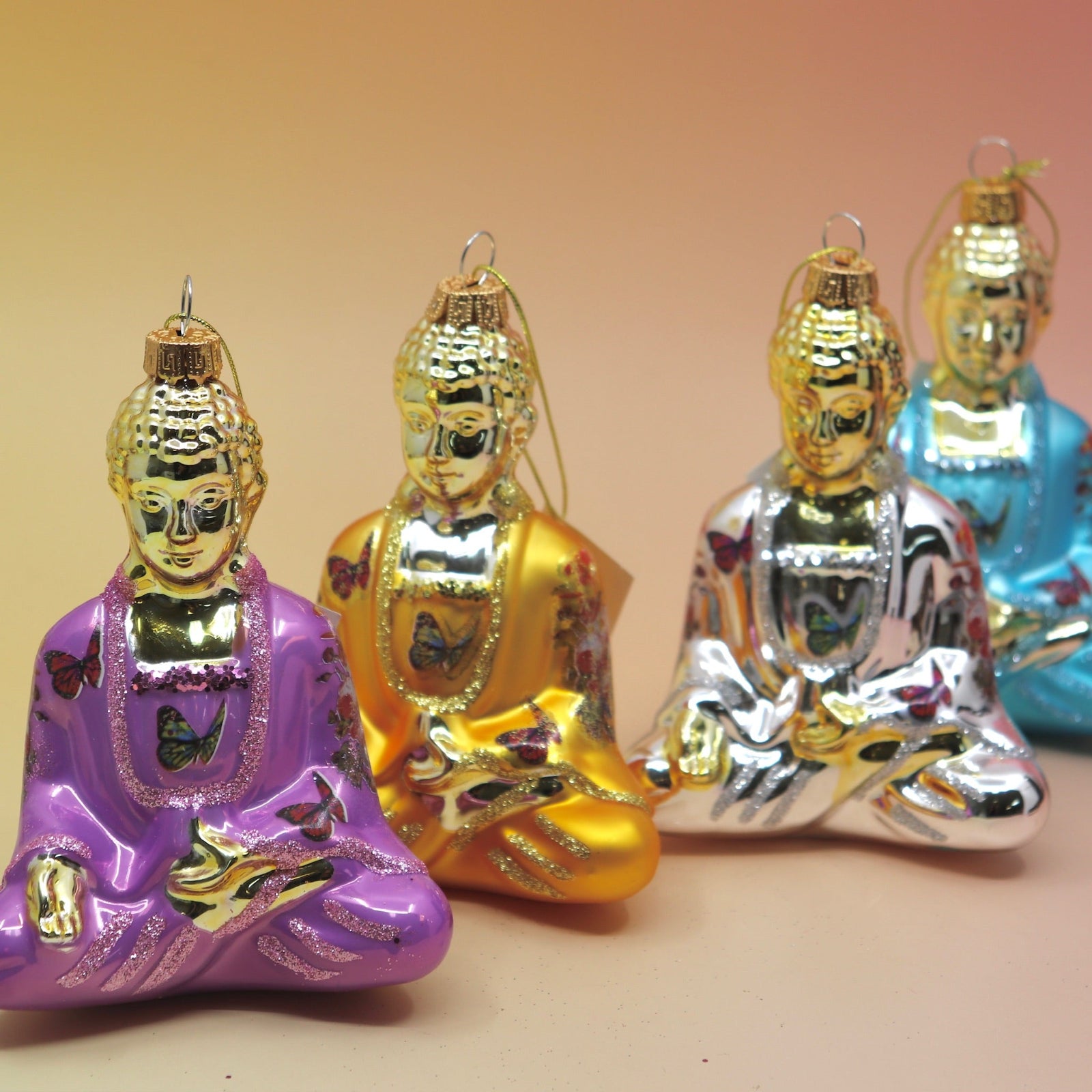 The four colors of the Buddha with Butterfly Glass Ornaments all on. apink and yellow background.