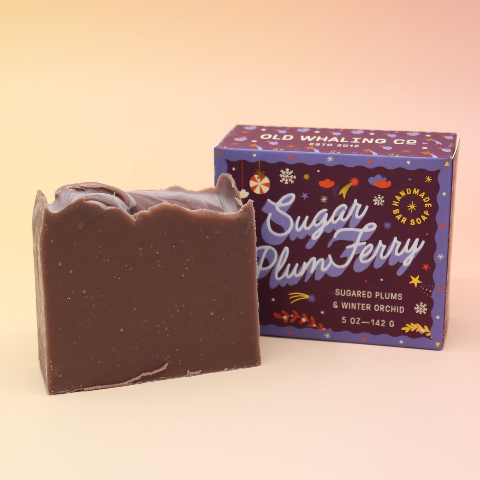 The Sugar Plum Ferry Holiday Bar Soap in front of its box on a pink and yellow background.