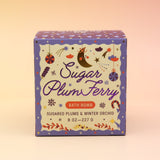 The Sugar Plum Ferry Holiday Bath Bomb in front of a pink and yellow background.