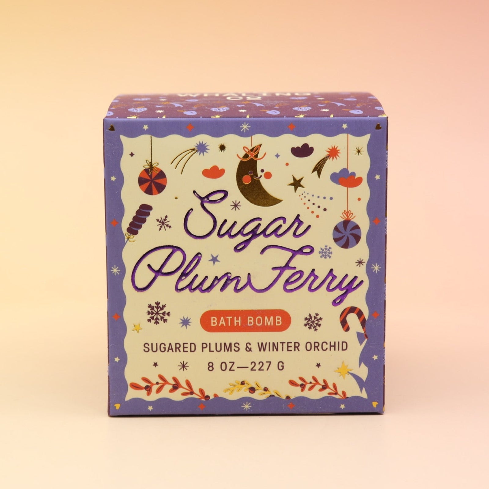 The Sugar Plum Ferry Holiday Bath Bomb in front of a pink and yellow background.