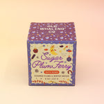 The Sugar Plum Ferry Holiday Bath Bomb in front of its box, all on a pink and yellow background.