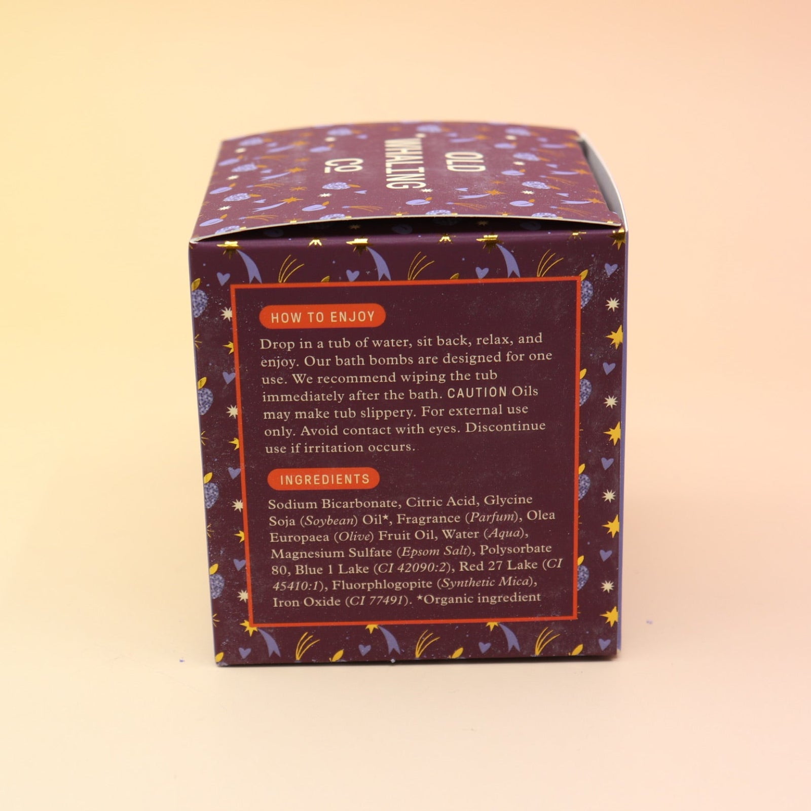 The Sugar Plum Ferry Holiday Bath Bomb in front of a pink and yellow background, showing off the side.