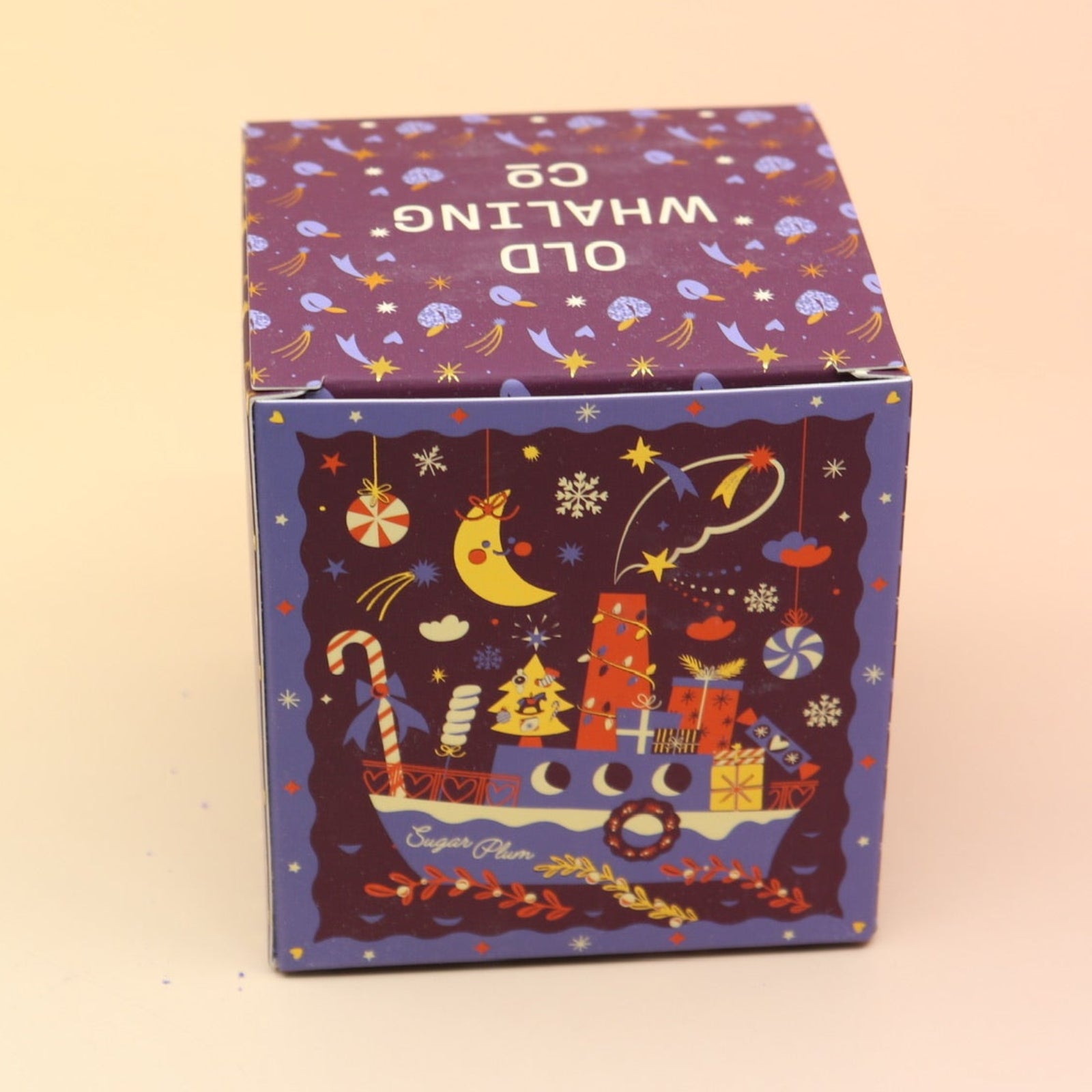 The Sugar Plum Ferry Holiday Bath Bomb in front of a pink and yellow background, showing off the side.