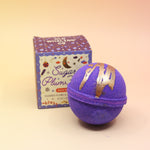 The Sugar Plum Ferry Holiday Bath Bomb in front of its box, all on a pink and yellow background.