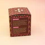 The Yuletide Glow Holiday Bath Bomb in front of a pink and yellow background, showing off the side.