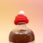 The red Mini Knit Cap on top of a bottle on a pink and yellow background.