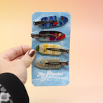 Someone holding the Tackle Box Fish Clip Set in front of a pink and yellow background.