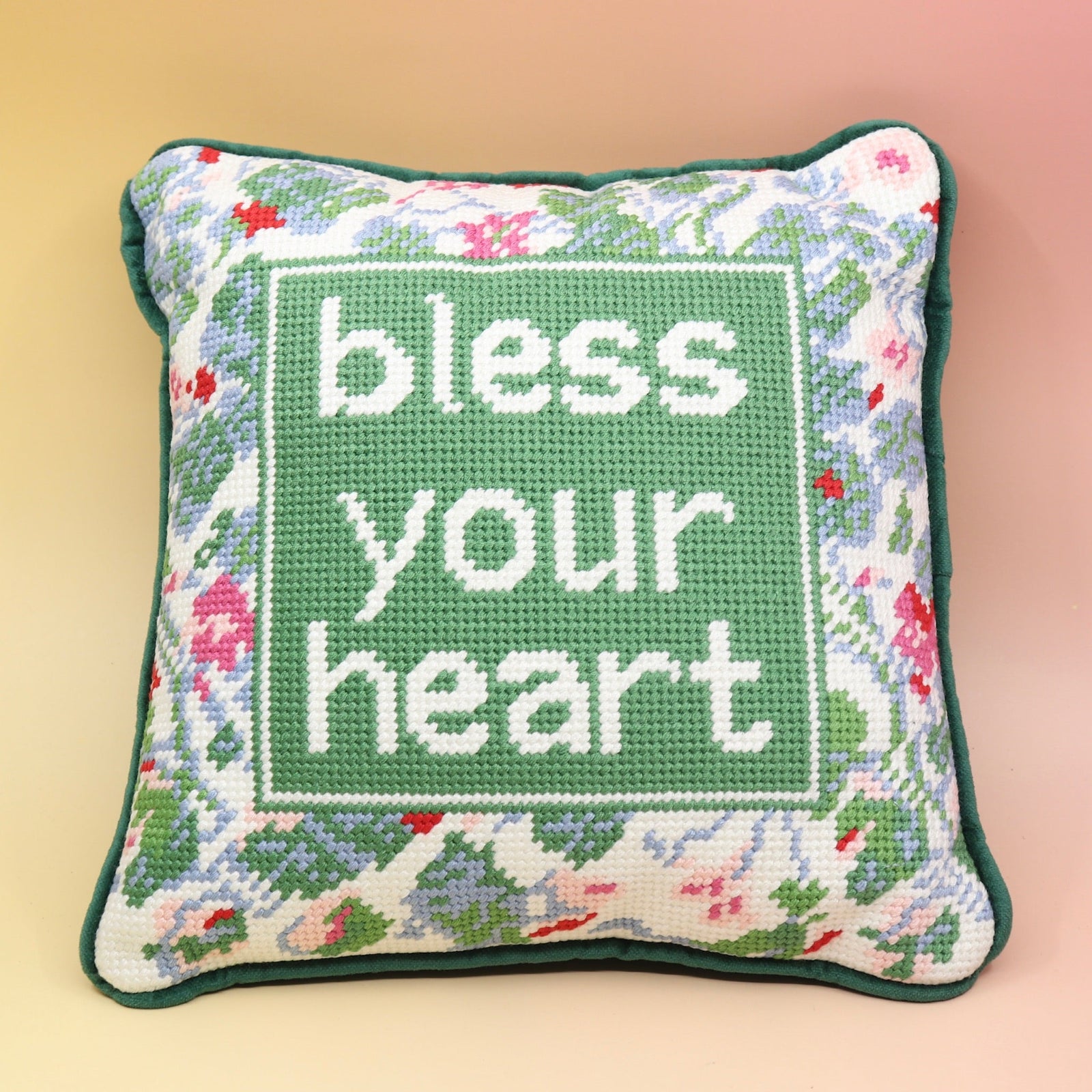 The Bless Your Heart Needlepoint Pillow on a pink and yellow background.