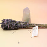 The Lavender Elixir Botanical Smudge Bundle in front of a crystal tower on a pink and yellow background.