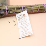 An up-close image of the Lavender Elixir Botanical Smudge Bundle in front of a crystal tower on a pink and yellow background.