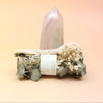 The Dreamy Eucalyptus Cleansing Smudge Bundle in front of a crystal tower on a pink and yellow background.