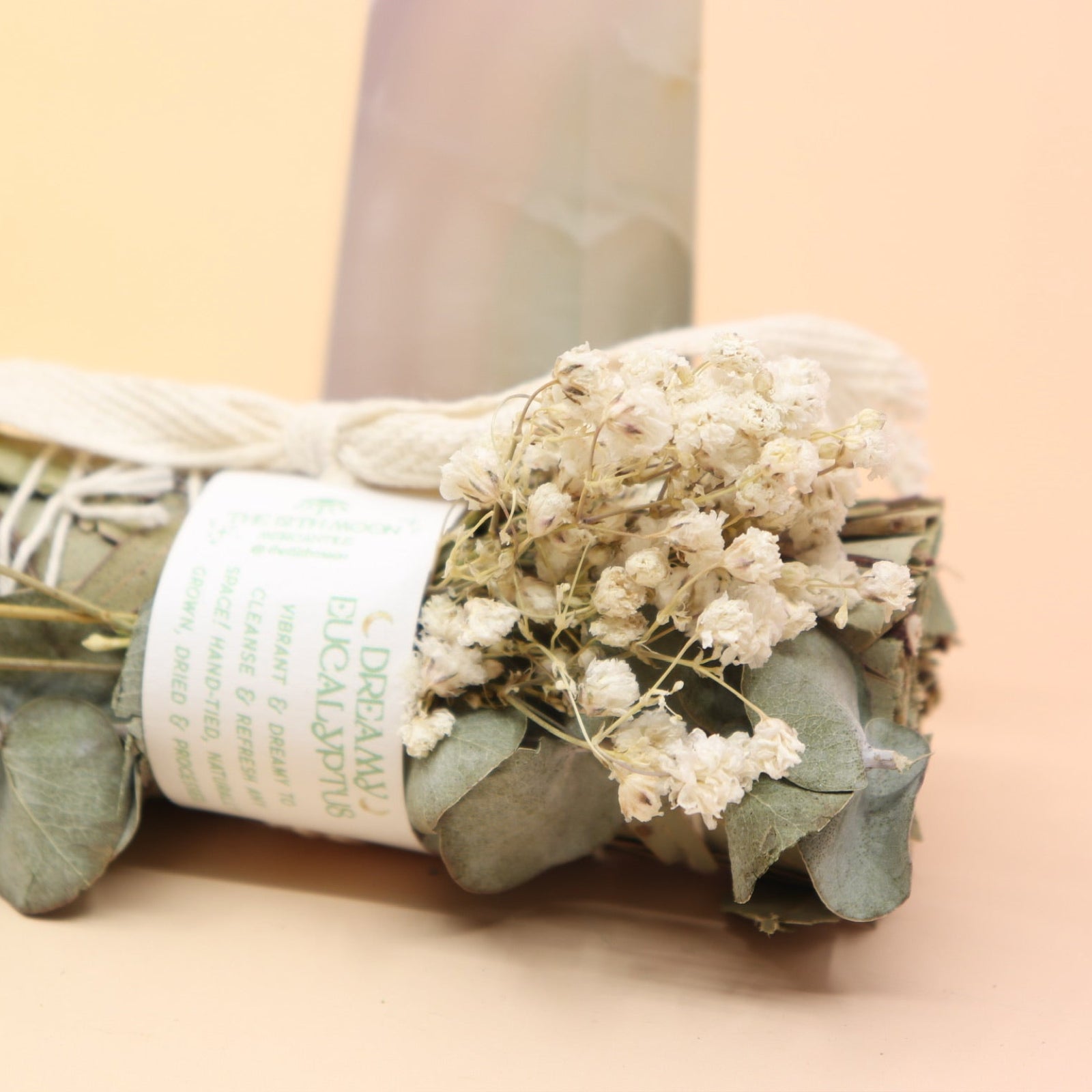 An up-close image of the Dreamy Eucalyptus Cleansing Smudge Bundle in front of a crystal tower on a pink and yellow background.