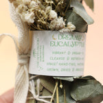 An up-close image of the Dreamy Eucalyptus Cleansing Smudge Bundle in front of a crystal tower on a pink and yellow background.