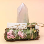 The Selenite Thyme Cleansing Smudge Bundle in front of a crystal tower on a pink and yellow background.