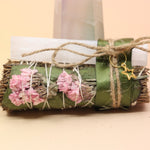 The Selenite Thyme Cleansing Smudge Bundle in front of a crystal tower on a pink and yellow background.