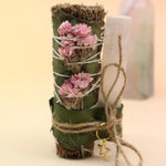 The Selenite Thyme Cleansing Smudge Bundle in front of a crystal tower on a pink and yellow background.
