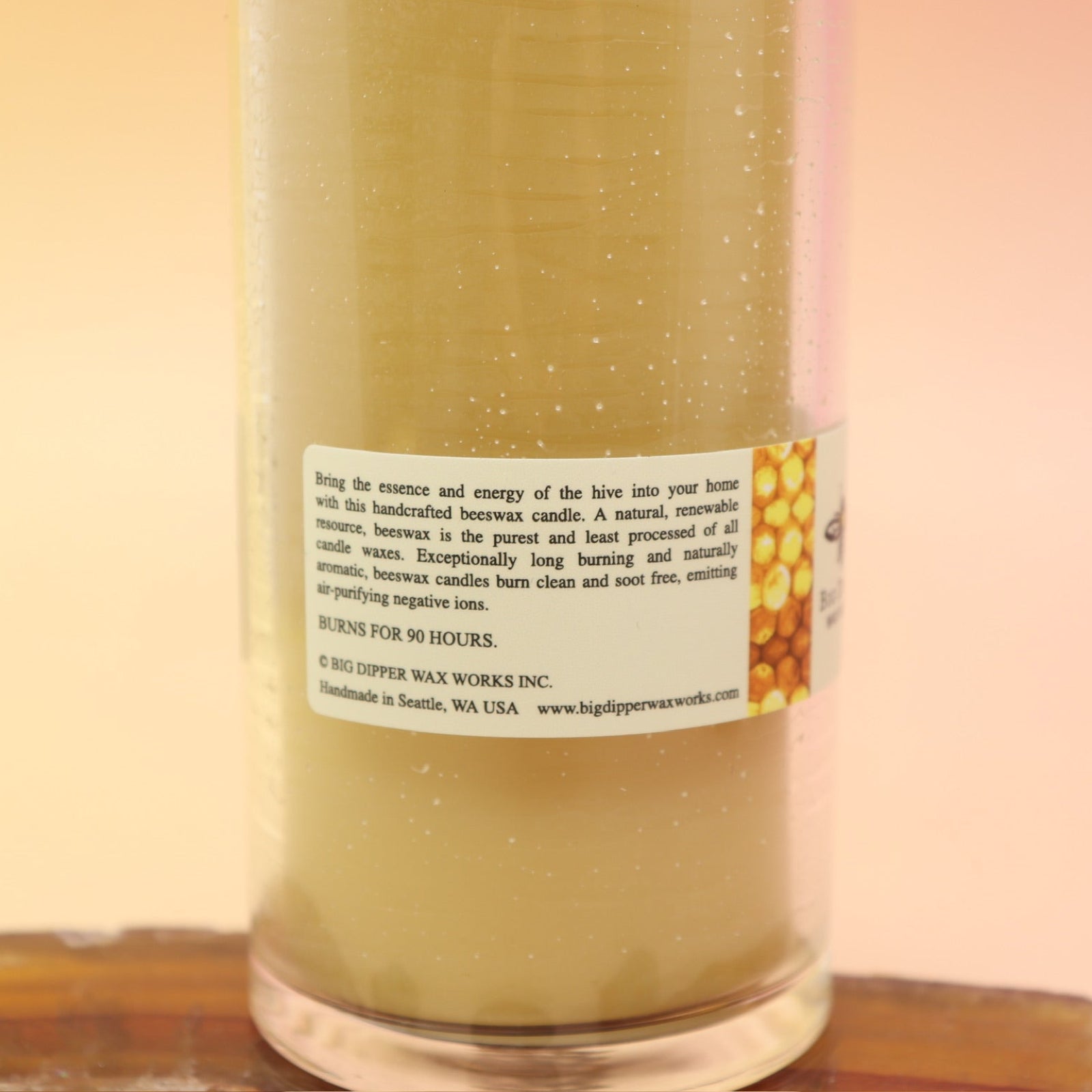 An up-close image of the Pure Beeswax Sanctuary Glass Candle on an agate slice all on a pink and yellow background, showing off the back.