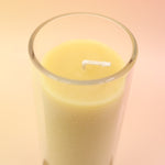 The Pure Beeswax Sanctuary Glass Candle on a pink and yellow background.