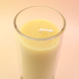 The Pure Beeswax Sanctuary Glass Candle on a pink and yellow background.