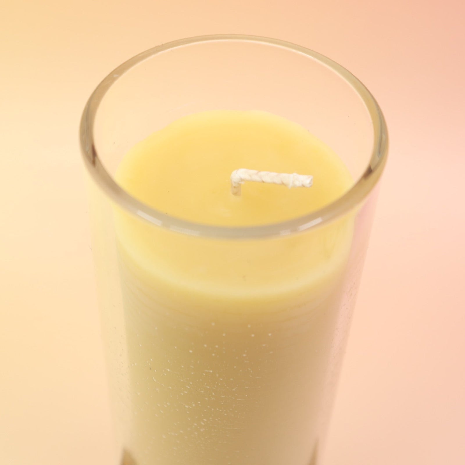 The Pure Beeswax Sanctuary Glass Candle on a pink and yellow background.