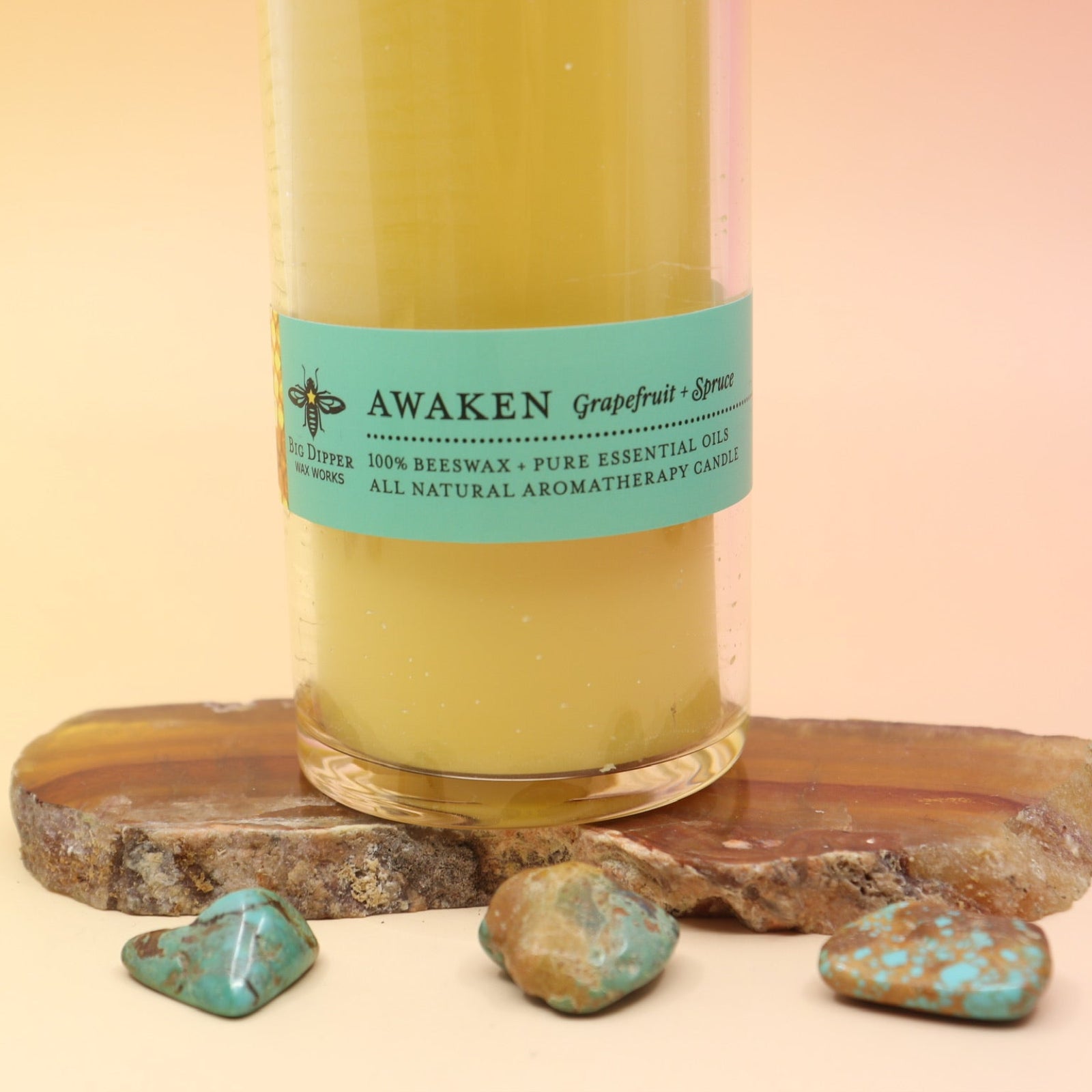 The Awaken Beeswax Aromatherapy Sanctuary Glasses on an agate slice all on a pink and yellow background.
