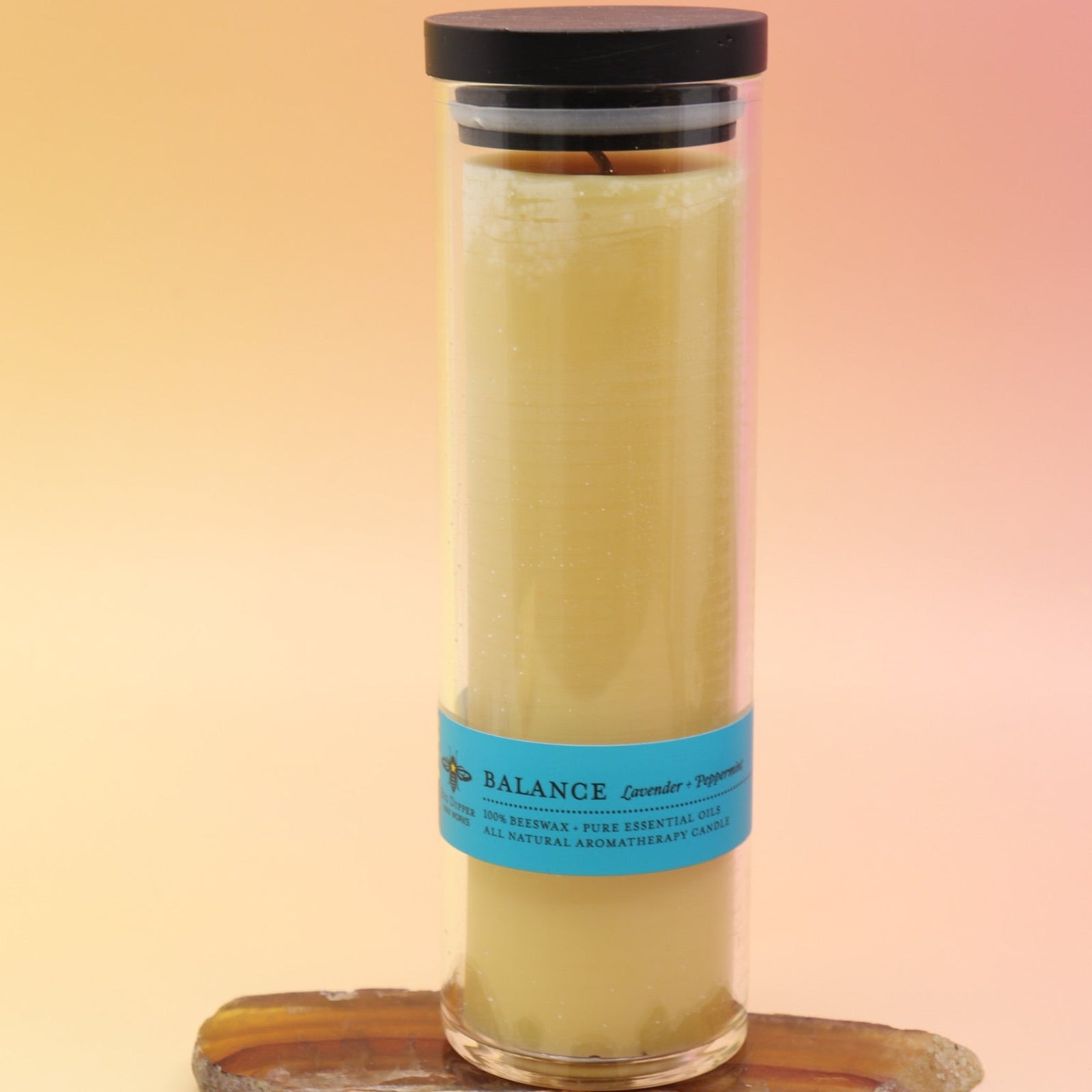 The Balance Beeswax Aromatherapy Sanctuary Glasses on an agate slice all on a pink and yellow background.