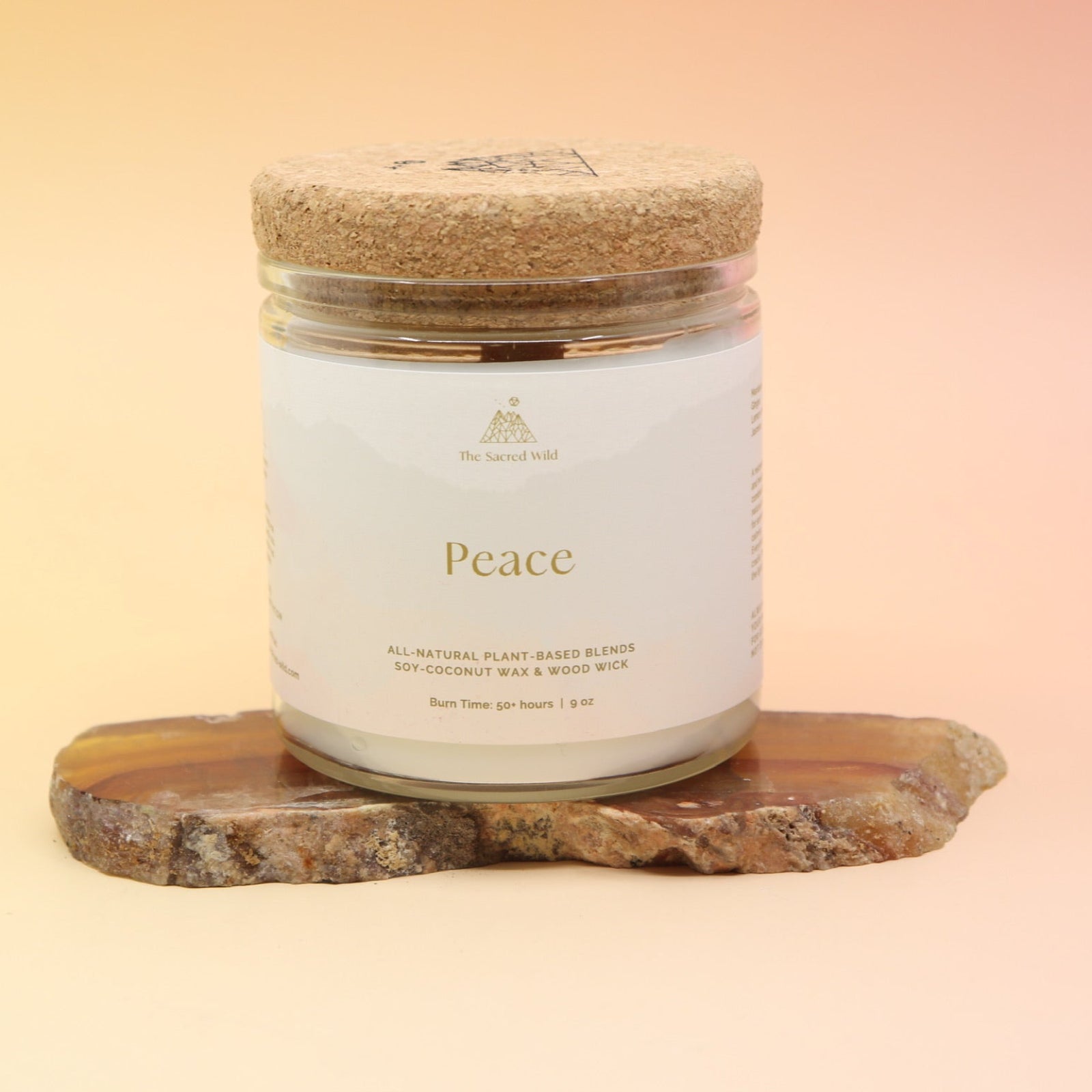 The medium Peace Intention Candle on an agate slice all on a pink and yellow background.