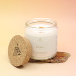 The large Peace Intention Candle on an agate slice all on a pink and yellow background, with the cork lid off.