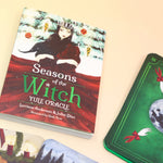 The contents of the Seasons of the Witch Yule Oracle Card Deck on a pink and yellow background.