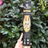 Someone holding the Krampus Premium Incense in front of a green bush.