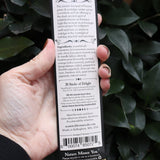 An up-close of image someone holding the Krampus Premium Incense in front of a green bush, showing off the back