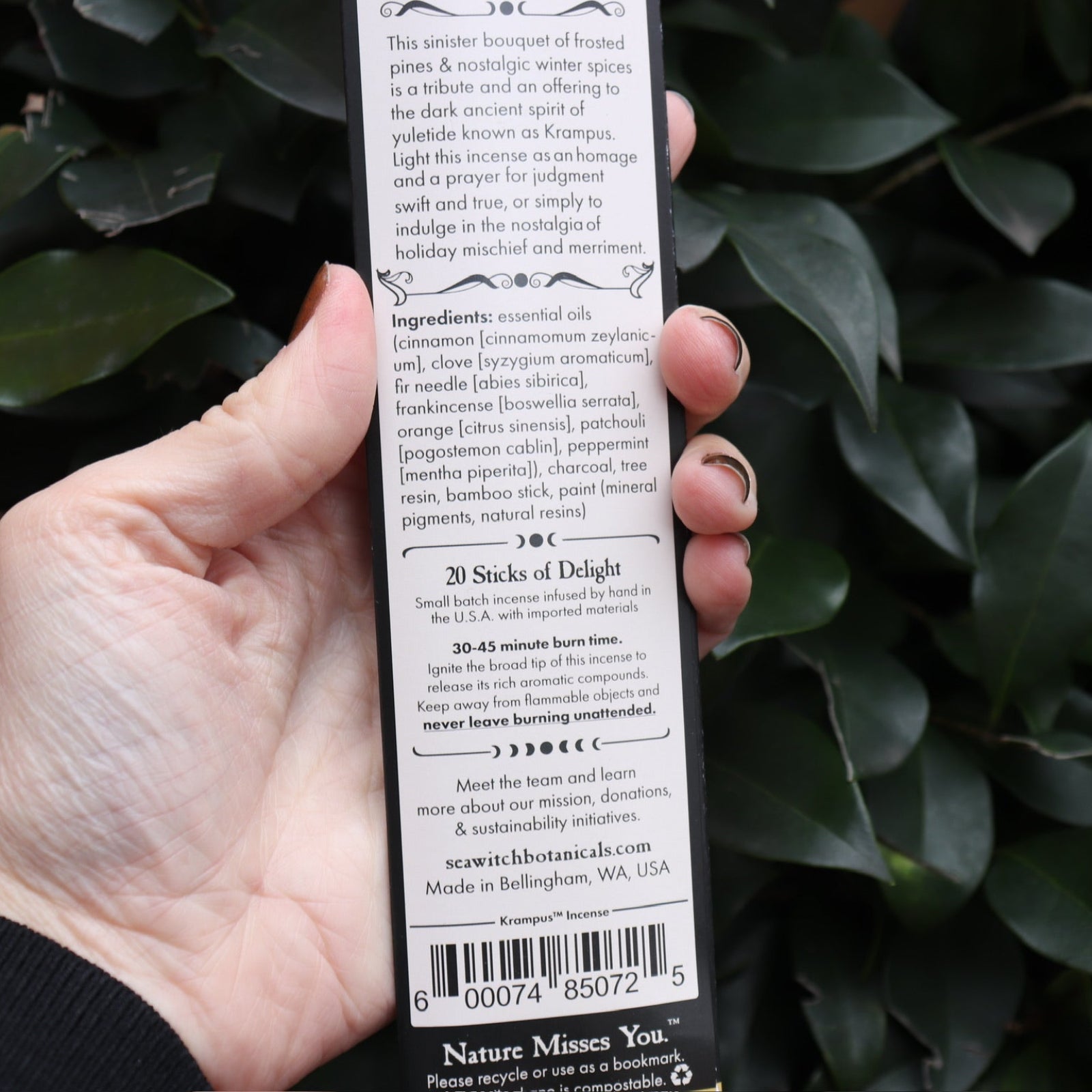 An up-close of image someone holding the Krampus Premium Incense in front of a green bush, showing off the back