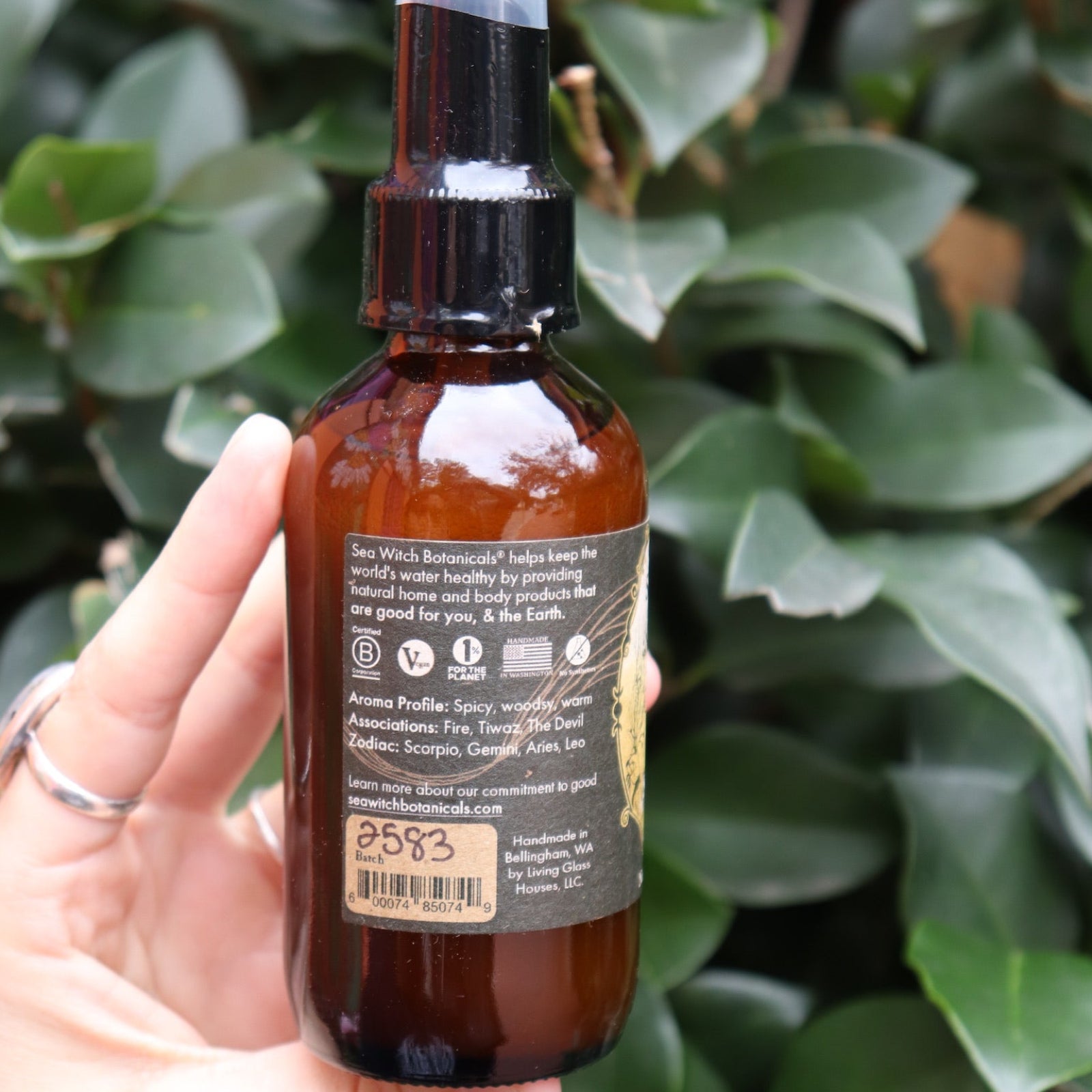 Someone holding the Krampus Scented Veil Spray in front of a green bush.