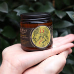 Someone holding the Krampus Soy Wax 3 oz Candle in front of a green bush.
