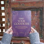 Someone holding the Find Your Goddess Paperback Book in front of a wood background.