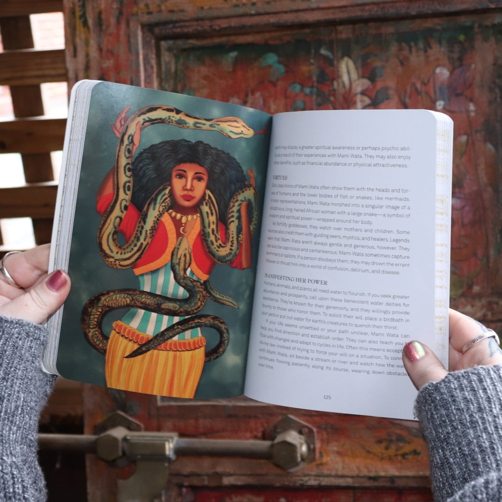 Someone holding the Find Your Goddess Paperback Book open in front of a wood background, showing off some pages.