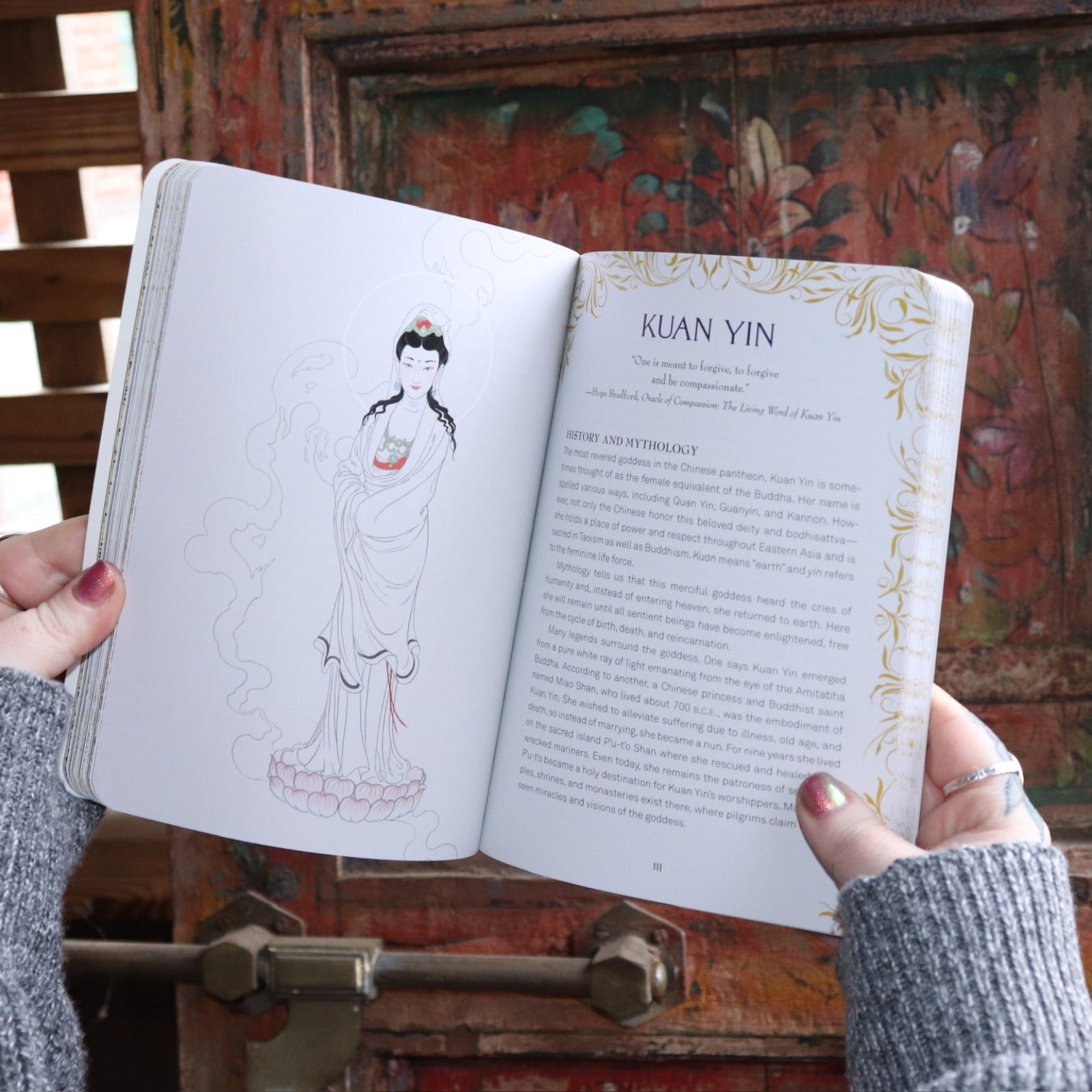 Someone holding the Find Your Goddess Paperback Book open in front of a wood background, showing off some pages.