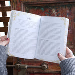 Someone holding the Find Your Goddess Paperback Book open in front of a wood background, showing off some pages.