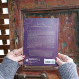Someone holding the Find Your Goddess Paperback Book in front of a wood background, showing off the back.